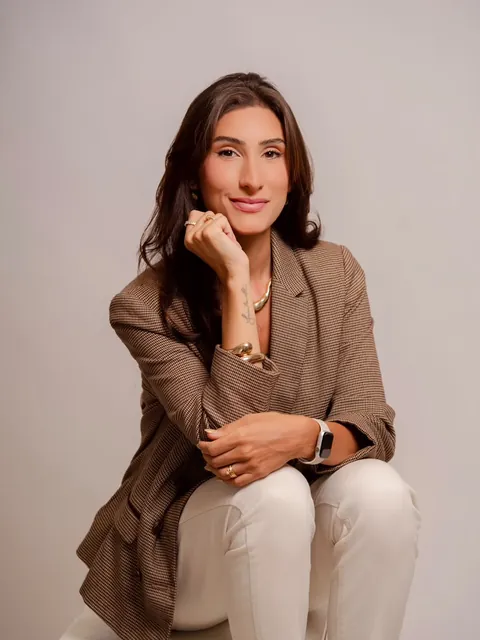 Natália de blazer, com a mão no queixo